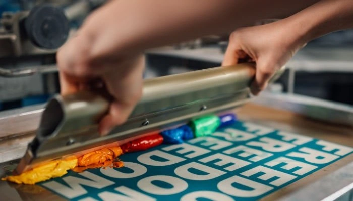 An image of a screen printing process showing two hands spreading colored matter on a stencil