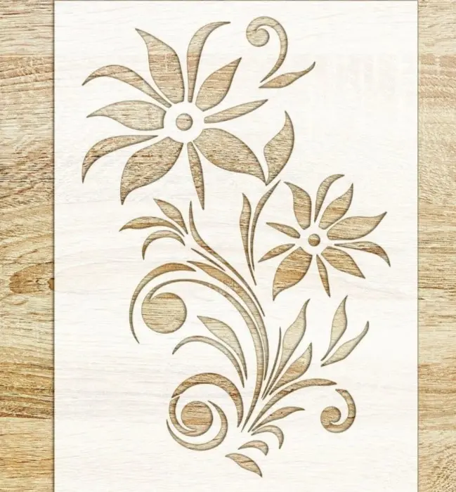 A flowery design on a white polypropylene stencil on a wooden surface