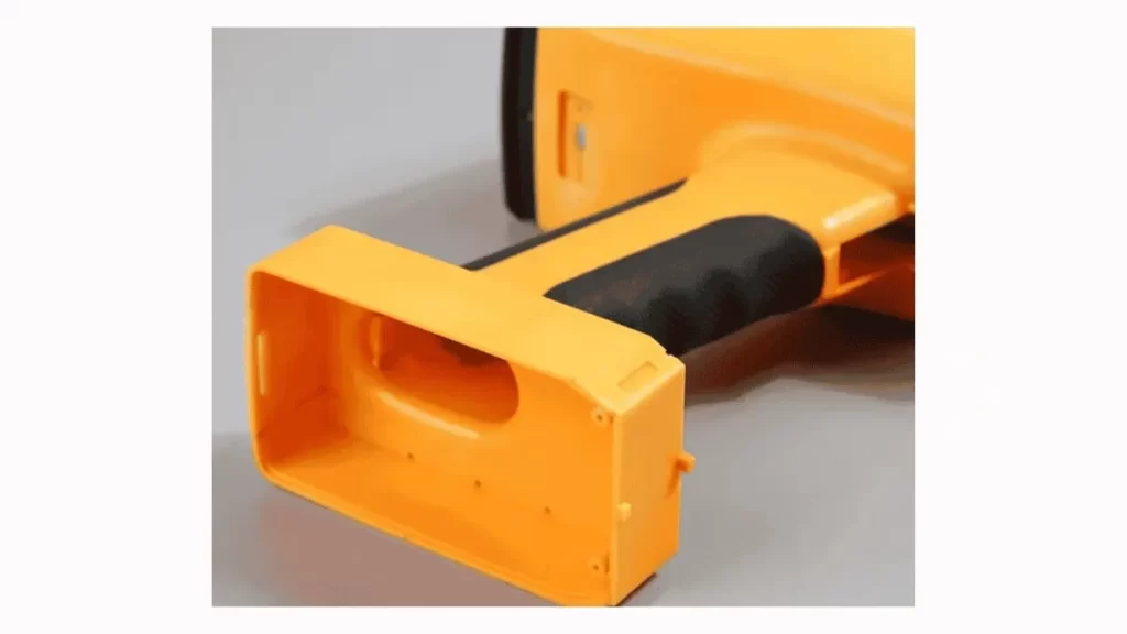 The image is an orange and black overmoulded part designed for testing, looking like an electronic device enclosure.