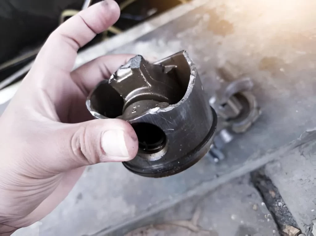 A Close-up view of an engine piston broken due to imperfect lubrication, held by an operator.