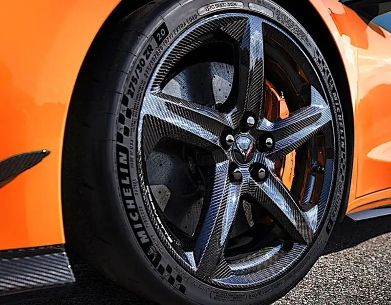A closeup of a carbon fiber wheel on an orange sports car with Michelin tires