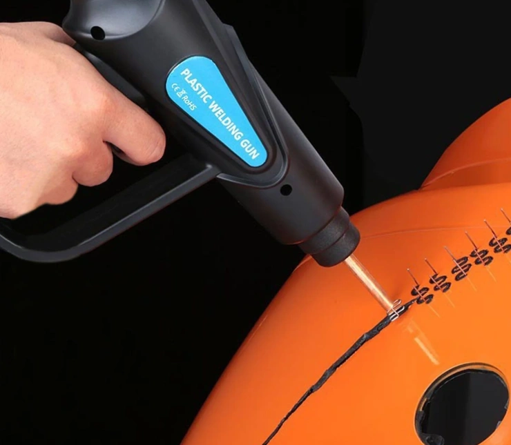 A person using a plastic welding gun to repair a crack in the bumper of a yellow car