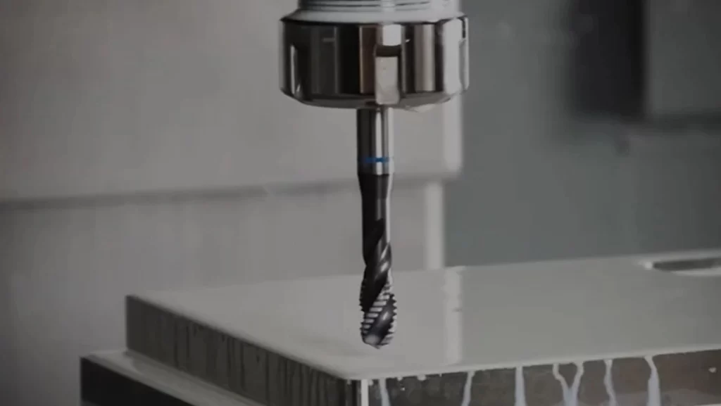 A close-up of a drill bit entering a material, creating a spray of liquid and debris.