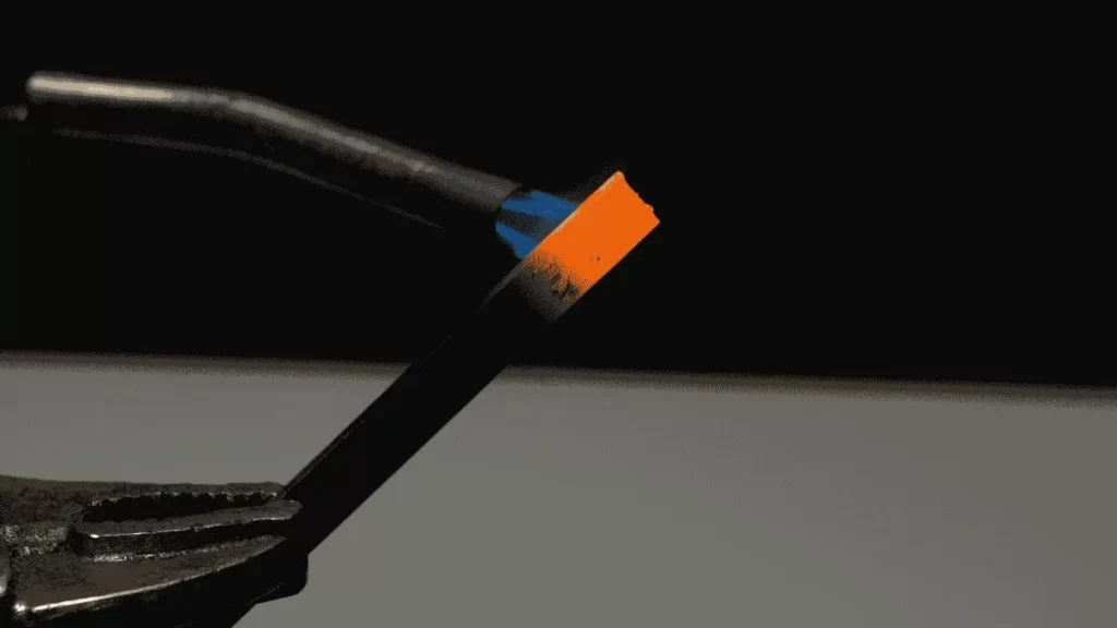 A person holding a hot piece of tool steel and cooling it after heat treatment, with visible heat glow on the metal.