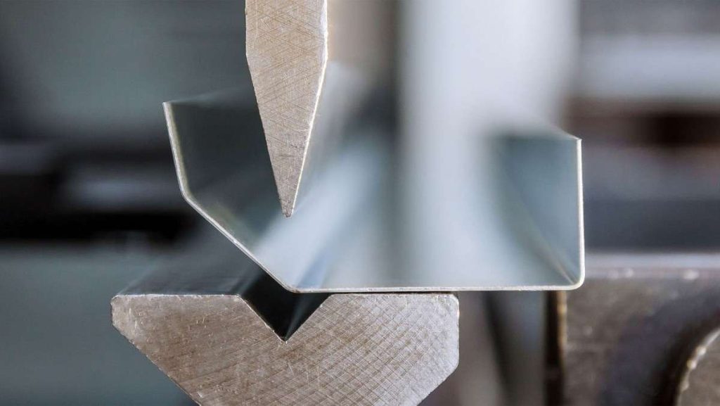 Close-up of a press brake bending a metal sheet into a channel shape.