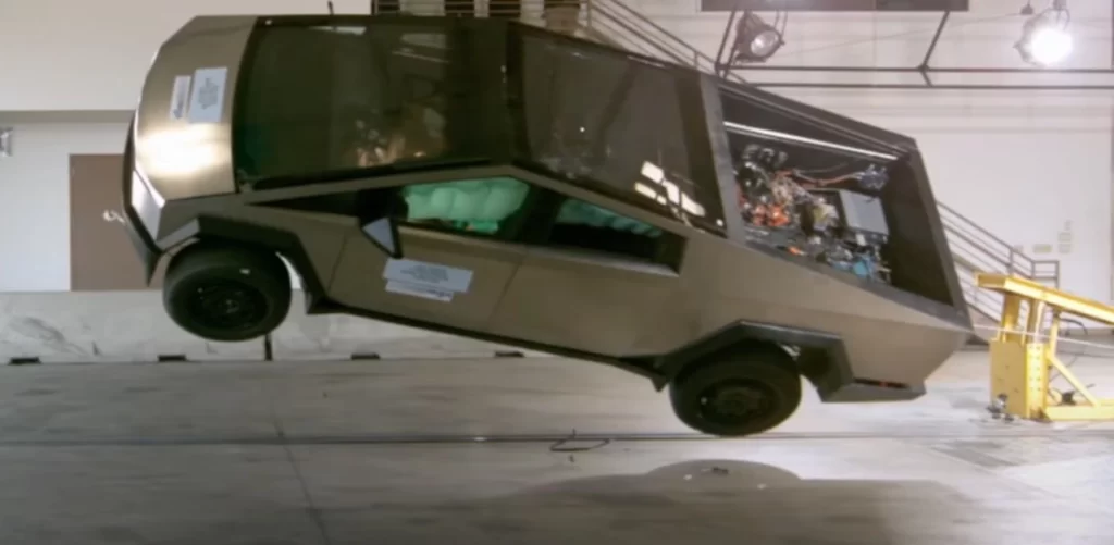 A silver Tesla’s cyber truck in an almost toppled position during a crash test in a well-lit space
