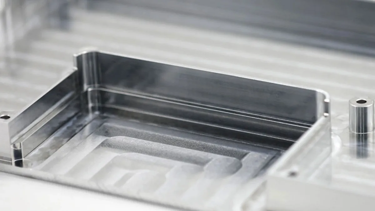 A machined aluminium pocket component sitting on a machine table with sharp cut edges