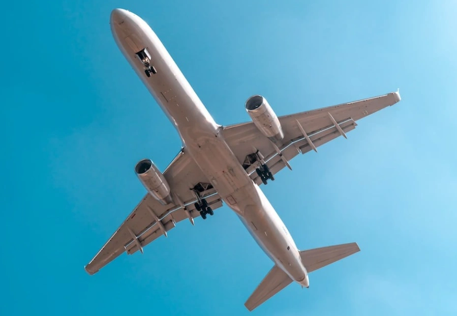 An image of an airborne white commercial aircraft taken from below showing a clear sky