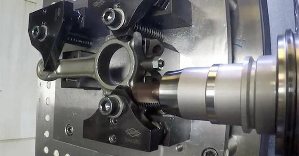 A CNC machine is finishing the connecting rod; the tool is spinning, and the rod is clamped in the vice. 