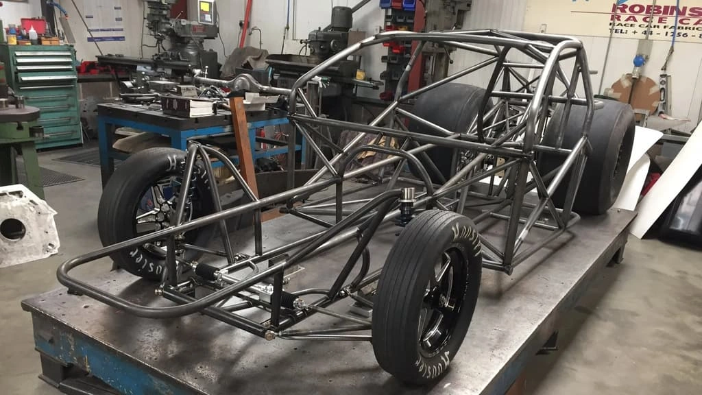 A close-up view of a workshop showing a tubular car frame on the ramp. 