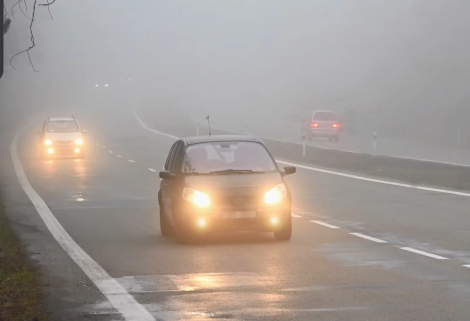 Cars driving with fog lights on through dense fog on a wet road with poor visibility conditions