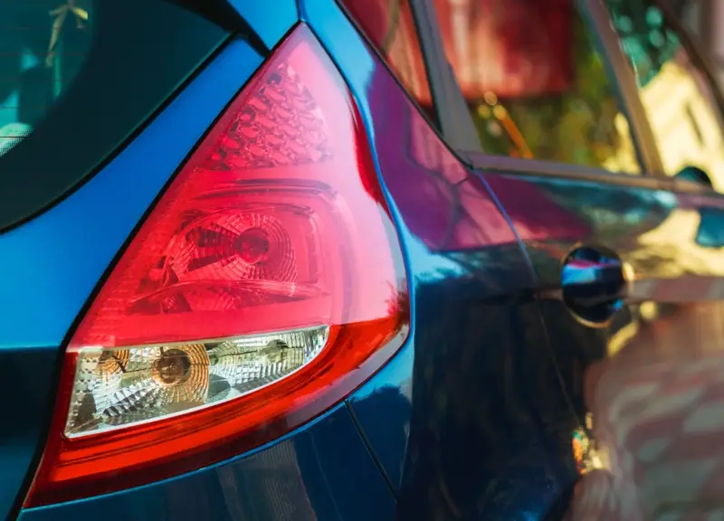 Red and clear PMMA tail light lens assembly on a blue car 