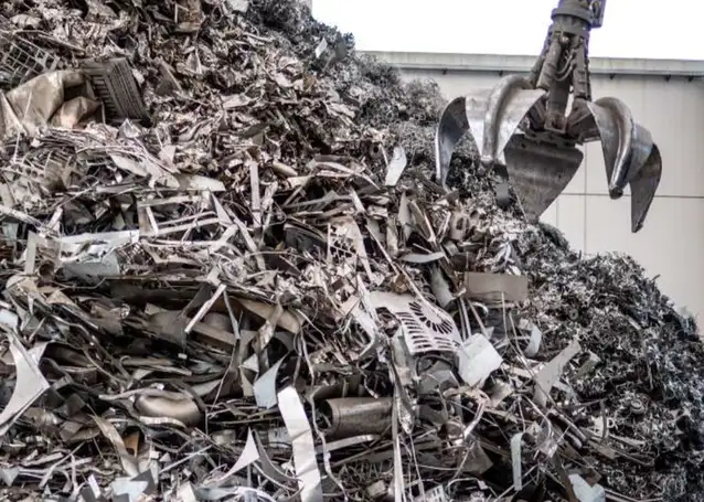 Industrial scrap metal yard with a large pile of ferrous metal waste and a mechanical claw grabber positioned above