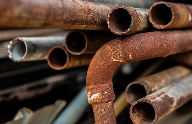 Stack of heavily rusted iron pipes showing various stages of corrosion and oxidation on their surfaces