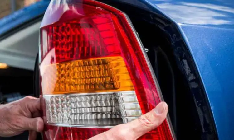Hand holding a tail light lens with red, amber, and clear textured plastic sections during replacement