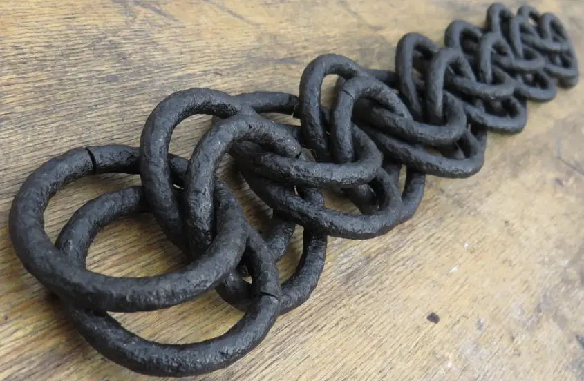 Heavy black wrought iron chain with thick interlocked links resting on a weathered wooden surface