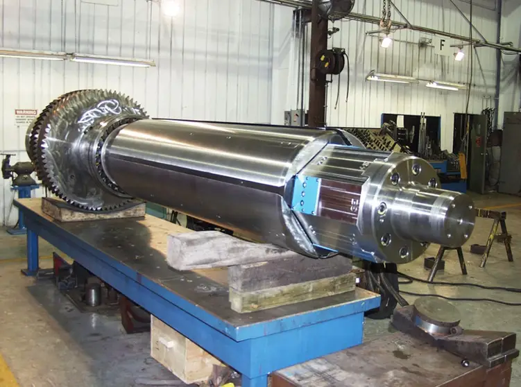 Large machined turbine rotor shaft with gear teeth on a blue assembly table in an industrial manufacturing facility