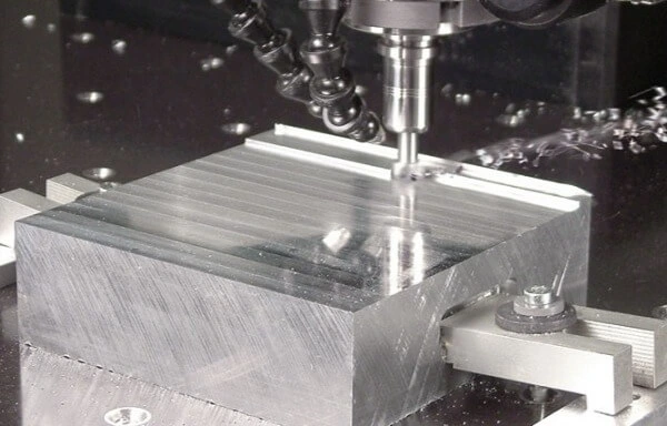 CNC milling machine cutting a block of aluminum with a flat end mill tool, showing surface finishing and precise machining