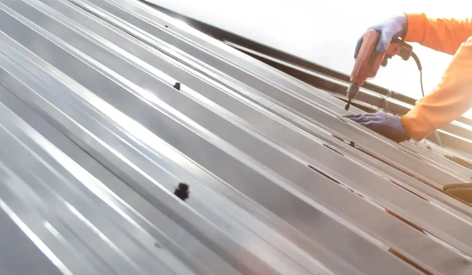 Worker installing joggled metal roofing panels with overlapping seams