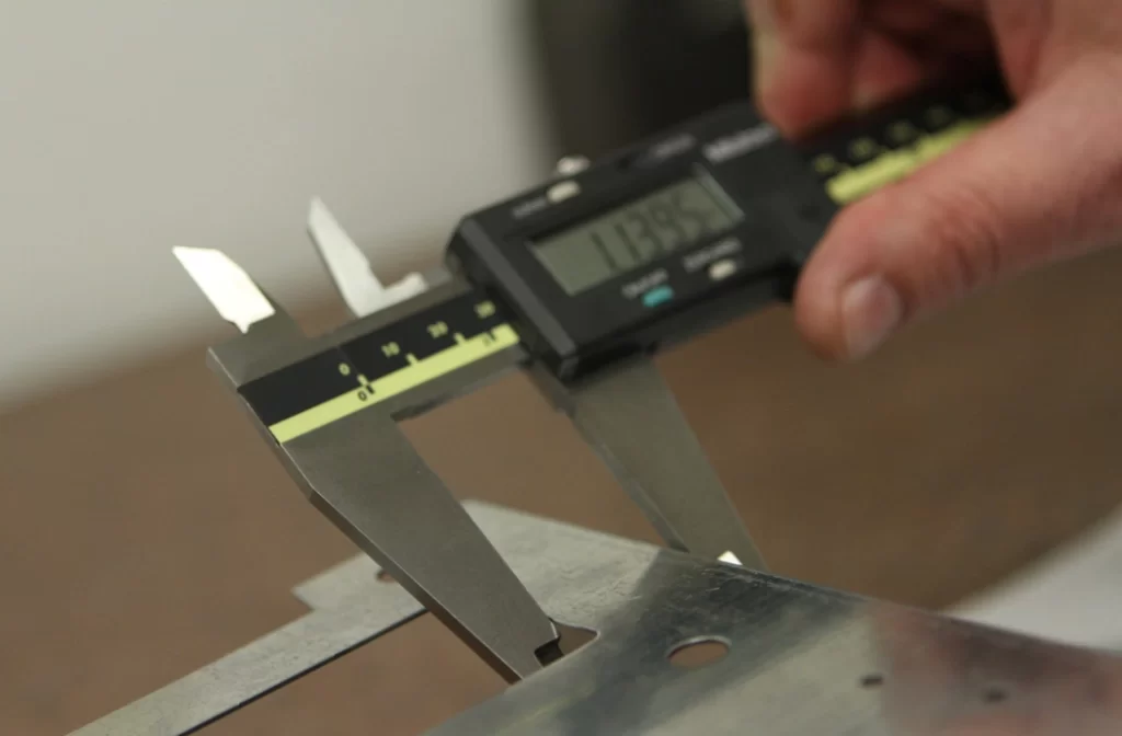 Digital caliper measuring the thickness of a steel blank with a punched hole