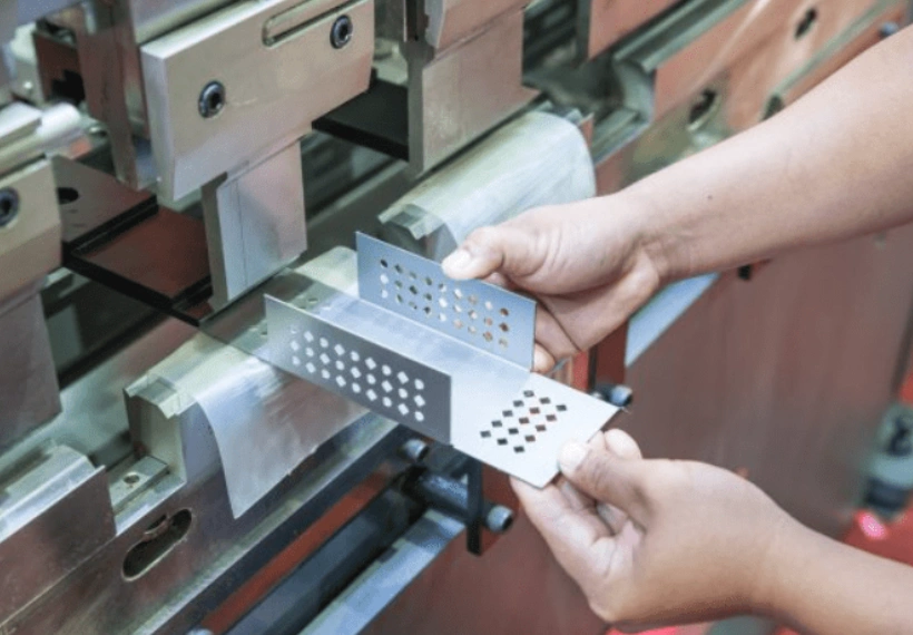 Worker inspecting a perforated stainless steel stamped part at a press 