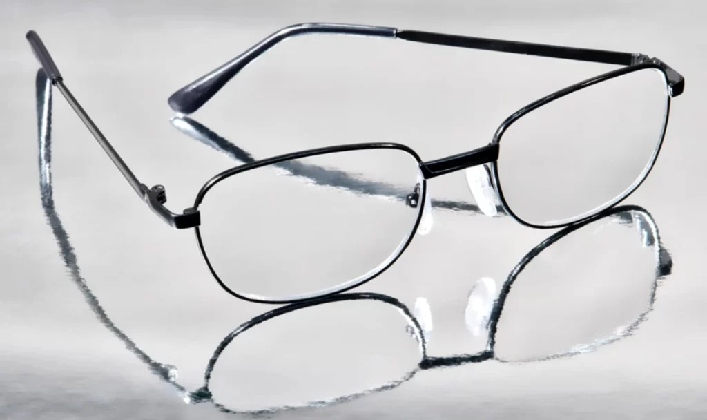 Eyeglasses with metal frames and polycarbonate lenses resting on a reflective surface