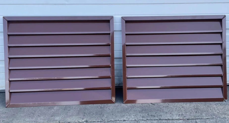 Two brown powder-coated aluminum louvers leaning against a white wall