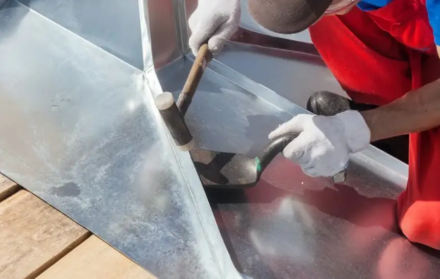 Worker manually bending sheet metal using a hammer and forming tools