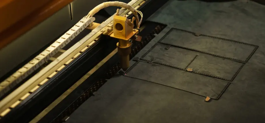 CO2 laser head engraving and cutting detailed rectangular patterns into dark genuine leather on a honeycomb bed during laser cutting materials process.