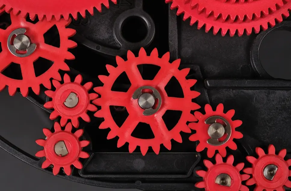 Red nylon gears with metal shafts meshed on a black plastic housing, an application where nylon heat resistance may be put to the test