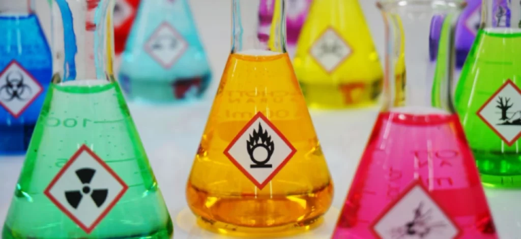 Polycarbonate laboratory flasks containing colorful chemicals with hazard warning labels