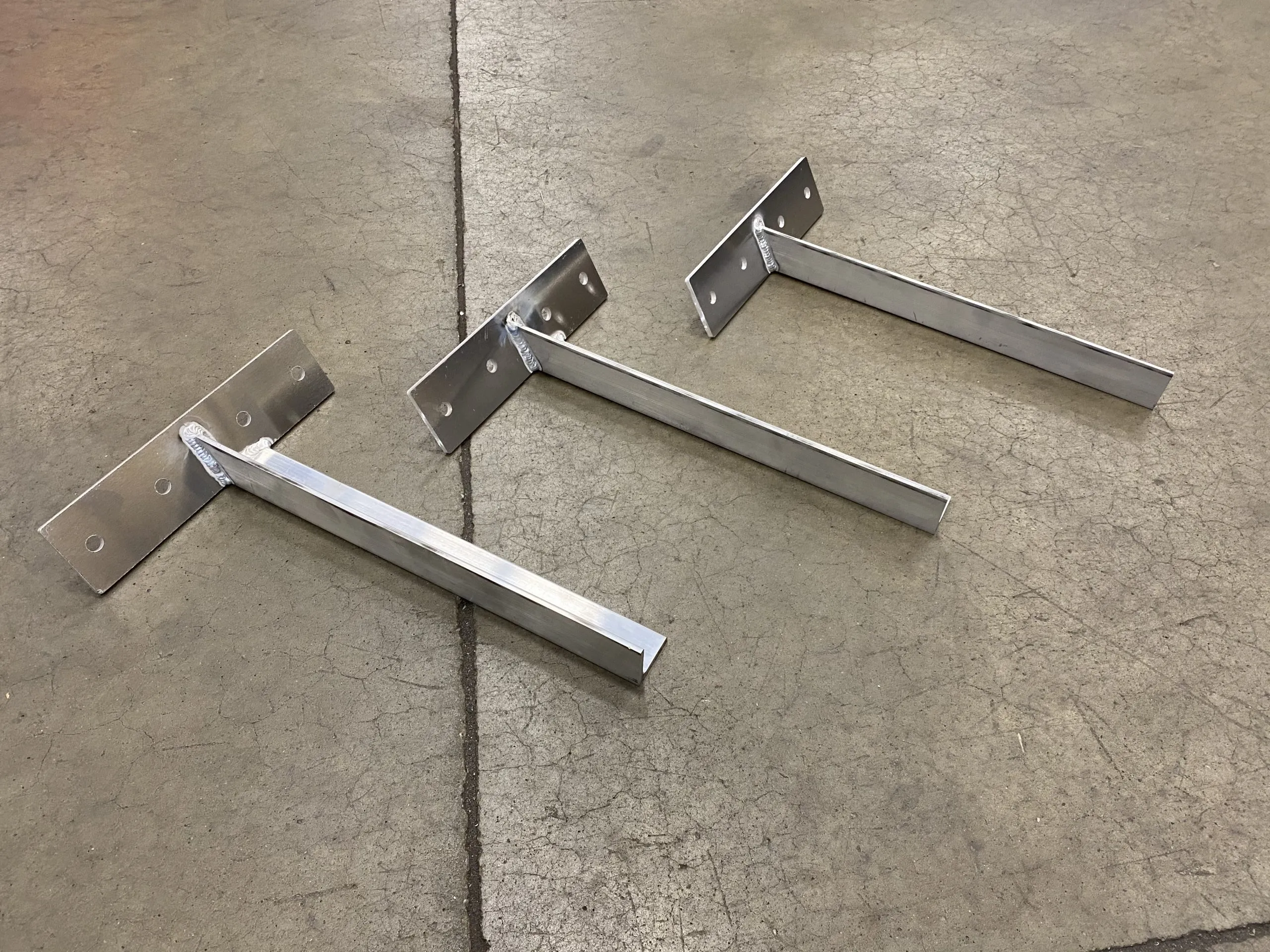 Three metallic T-shaped parts lying horizontally on a rough-textured shelf