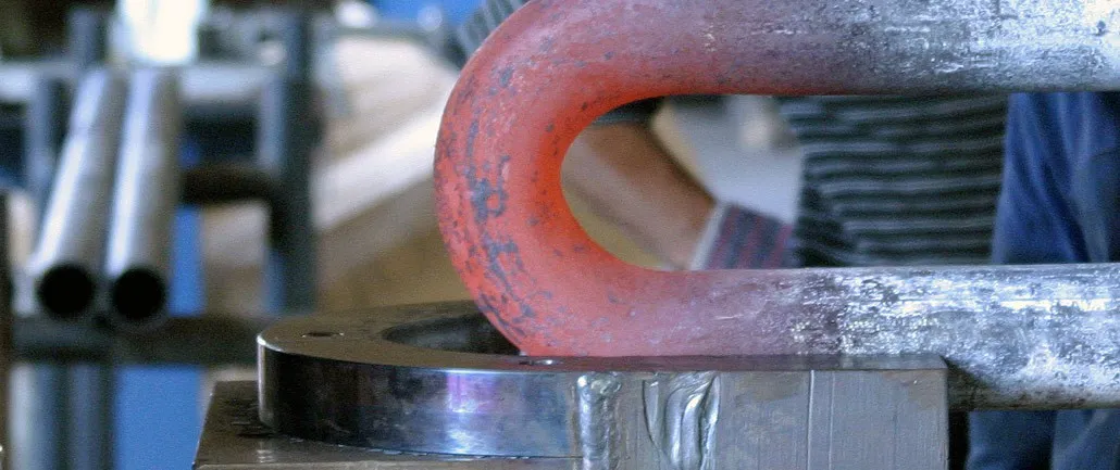 A red-hot titanium pipe while being in the process of bending in an industrial press machine