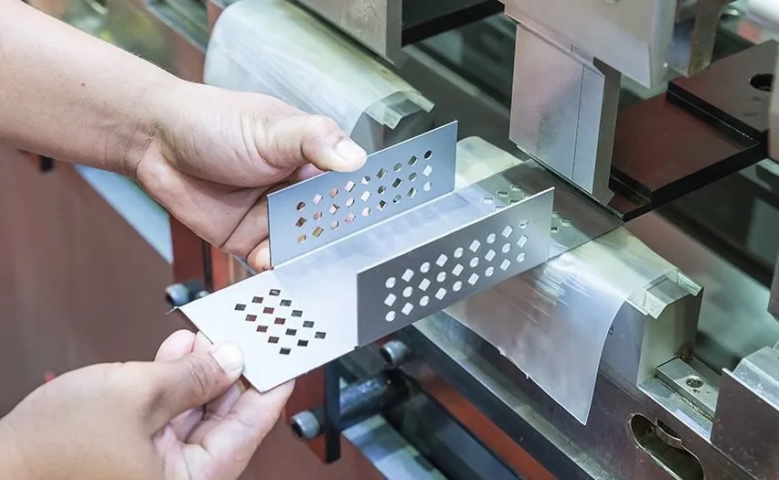Hands holding a bracket of titanium having diamond-shaped holes in it 