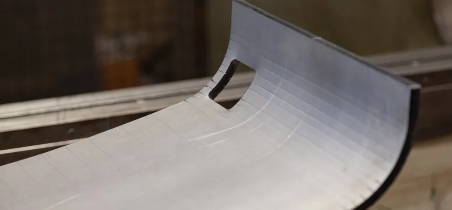 Close-up of a precision bump-formed sheet metal component featuring a smooth curved profile, rectangular cutout, and fine stepped forming lines.