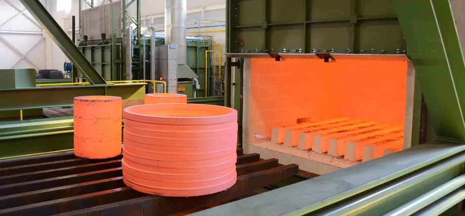 Industrial furnace with open door revealing glowing hot interior and red-hot cylindrical steel forgings on a conveyor