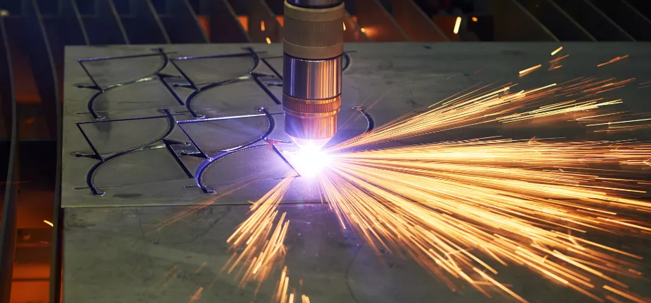 Plasma cutter torch actively cutting intricate curved patterns in sheet metal with bright sparks and molten spray.