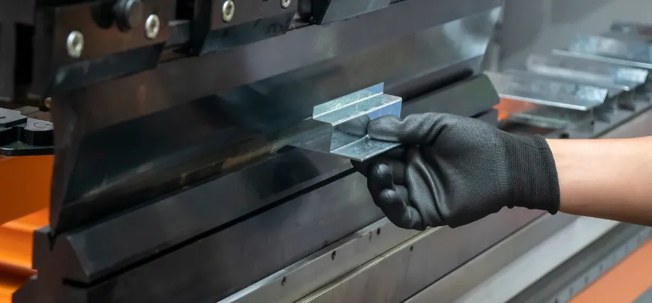 Gloved hand removing a freshly bent galvanized steel bracket from a press brake after forming a precise 90-degree flange.