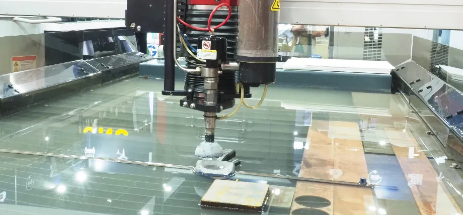 Waterjet cutting head actively piercing and cutting material on a submerged table with abrasive slurry and visible water surface ripples.