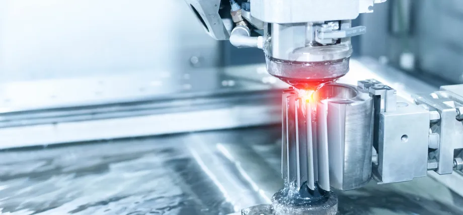 Close-up of an EDM machine using electrical discharges with a bright red spark to precisely cut a cylindrical metal workpiece in OEM metal fabrication