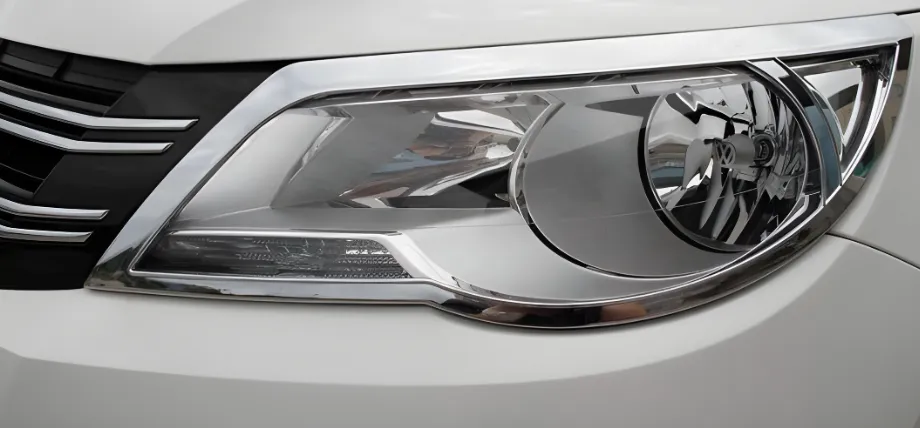 A close-up of a white vehicle's headlight assembly featuring a highly reflective decorative chrome-plated trim around the housing.