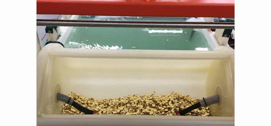 A specialized industrial barrel plating machine filled with small, gold-colored metal fasteners submerged in an electrolytic solution.