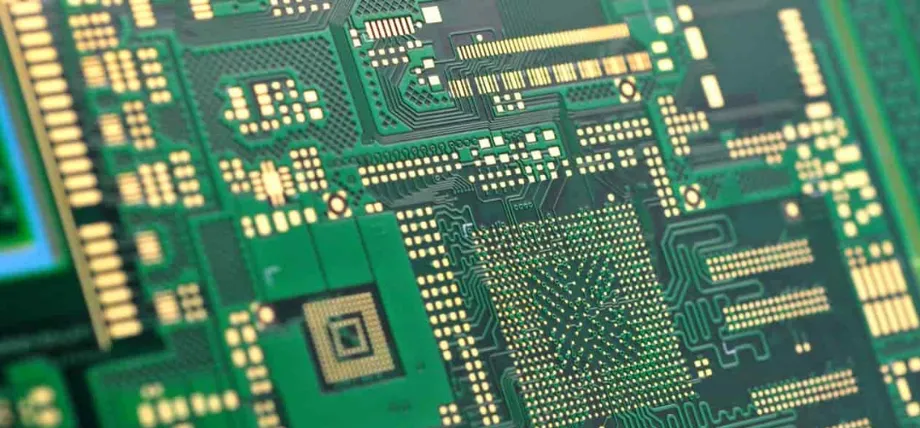 A macro view of a complex green printed circuit board (PCB) with intricate gold-plated contact pads and conductive copper traces.