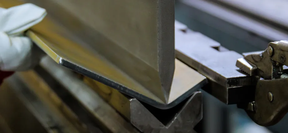 A gloved hand guiding a metal sheet into a press brake machine during the bending process