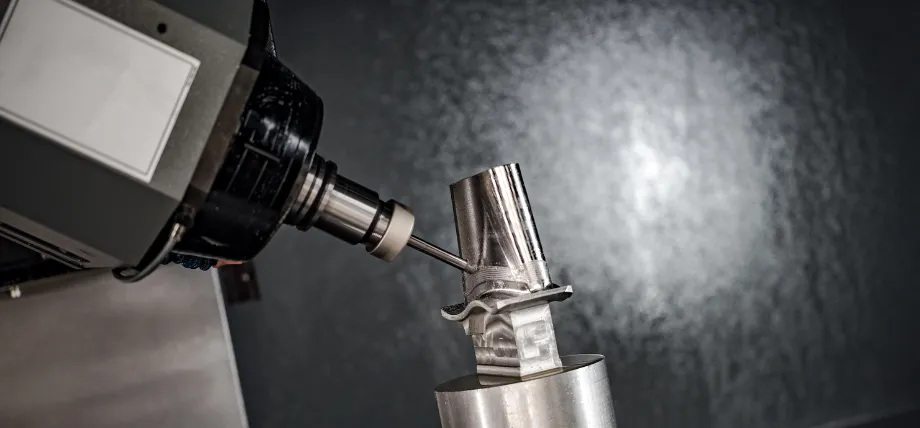 Close-up view of a CNC milling machine precisely cutting a shiny stainless steel workpiece with a coolant spray.