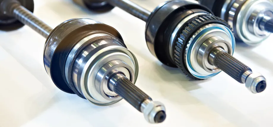Close-up view of several finished 4140 alloy steel drive shafts featuring splined ends, precision-machined journals, integrated flanges, and assembled roller bearings with black rubber seals.
