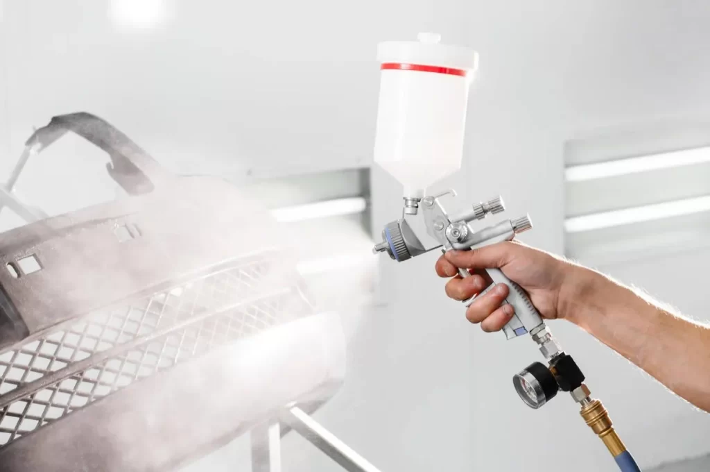 The image shows a man painting a blanked car part.