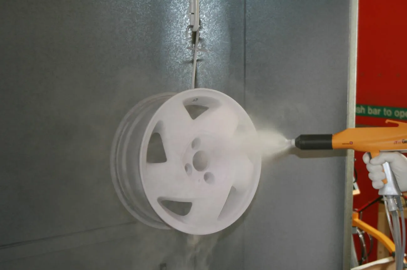 An alloy wheel being coated with dry powder from a hand-held electrostatic spray gun