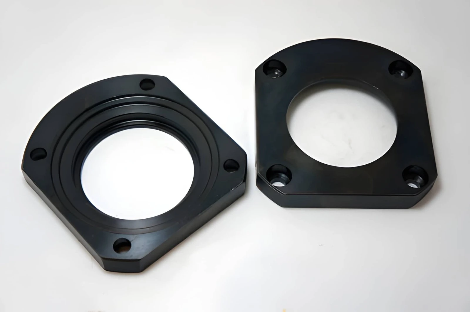 Two black oxide coated steel mounting brackets with a matte black surface