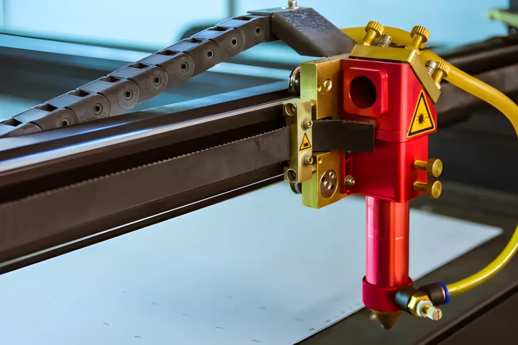 The image shows a CO₂ laser engraving machine with its cutting head idle inside a red metal body.
